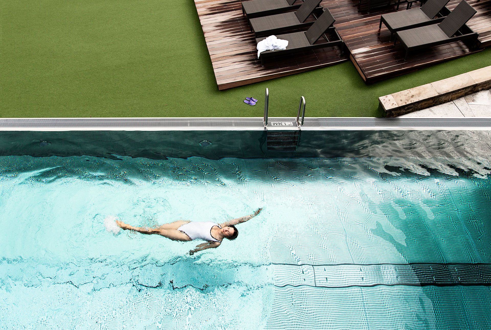 Blick von oben auf eine rückenschwimmende Frau im Outdoorpool des Hotels. Blick von oben auf eine rückenschwimmende Frau im Outdoorpool des Hotels.