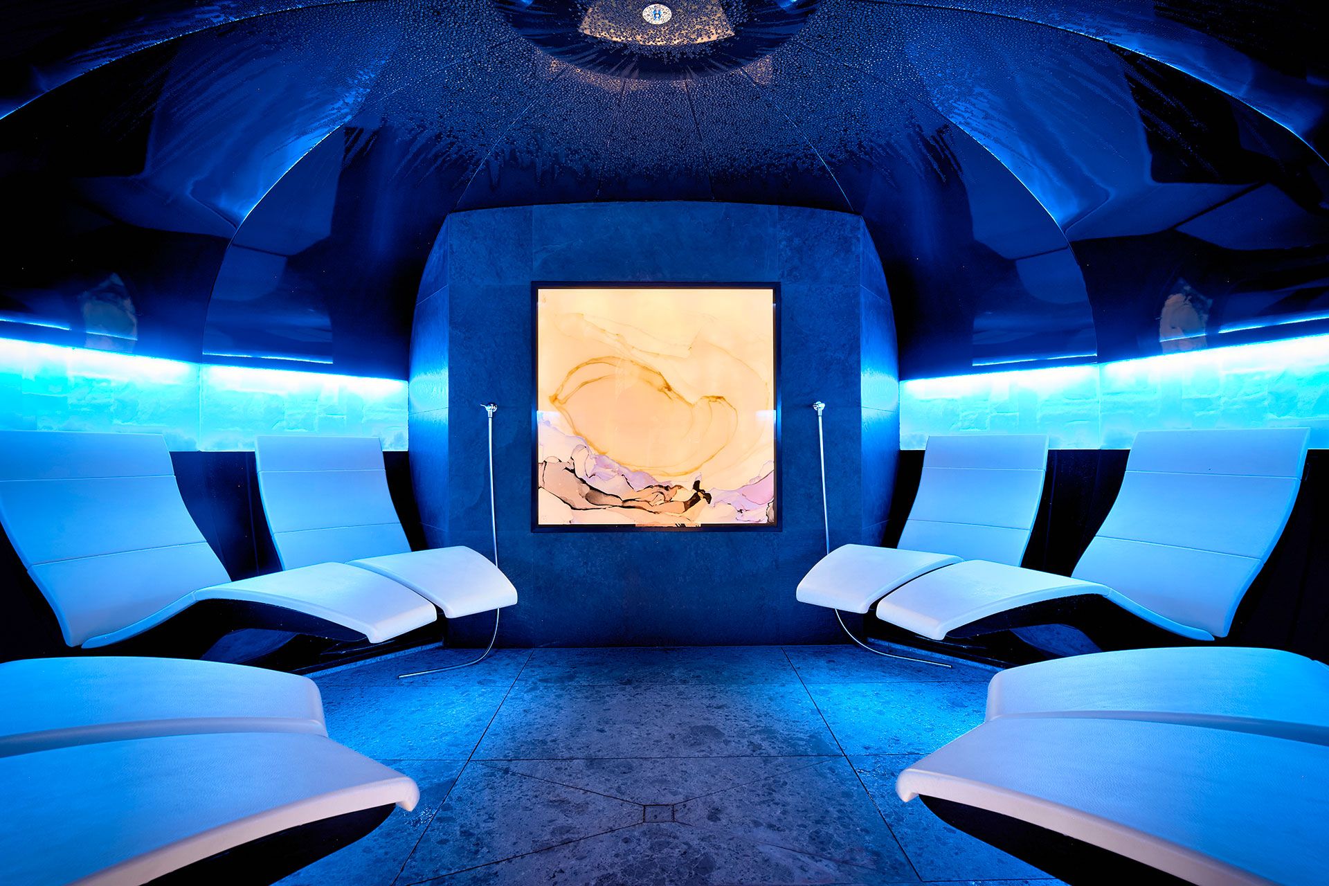 Abgedunkelter Wellnessbereich mit blauem Licht und acht Liegen zum Entspannen. Abgedunkelter Wellnessbereich mit blauem Licht und acht Liegen zum Entspannen.