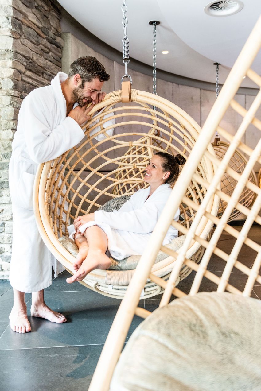 A happy couple in the wellness area, the woman sitting in a hanging round chair, the man standing beside her. A happy couple in the wellness area, the woman sitting in a hanging round chair, the man standing beside her.