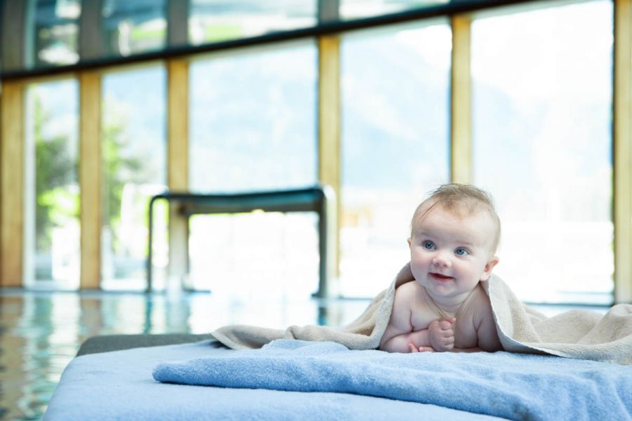 A happy baby, covered with a towel, lying on a wellness lounger. A happy baby, covered with a towel, lying on a wellness lounger.